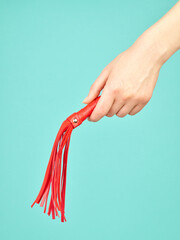 Red whip for adult role play games in woman's hand over turquoise blue background - 779789567