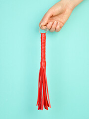 Red whip for adult role play games in woman's hand over turquoise blue background - 779789586