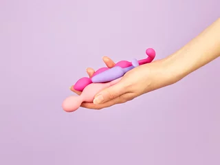 Tuinposter Woman's hand holding adult sex toys over violet background © Nik_Merkulov