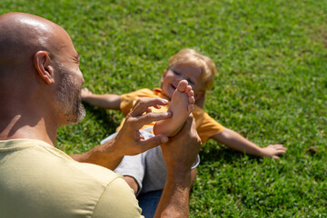 family and love concept - young father tickling his little son in park. close-up of a child's heel...