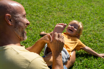 family and love concept - young father tickling his little son in park. dad tickles his son's legs...