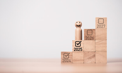 Wooden miniature figure smiling and standing on 2025 and correct tick mark for start and...