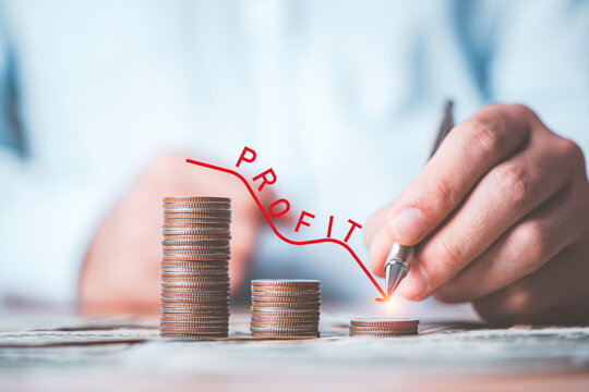 Businessman writing red down line with decreasing coins stacking for profit from business investment from economic depression crisis concept.