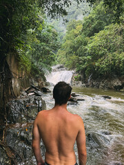 A man is standing in front of a waterfall, looking at the water