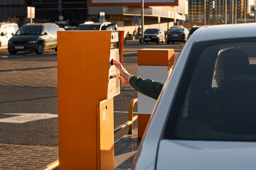 Man's hand take ticket in control tickets machine at vehicle entrance with boom barriers. Automatic barrier gates for supermarket parking lot. Security system for car park entry to shopping mall. © JinOdin