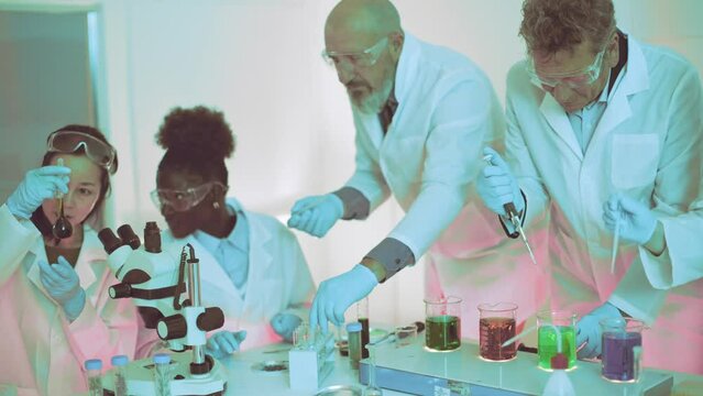 Scientific team engages in laboratory research - Protective eyewear and white lab coats standard as they utilize microscopes and pipettes