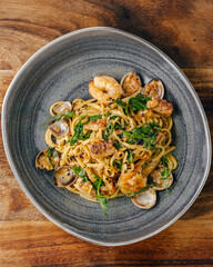 Elegant gray plate with pasta and seafood on a wooden table. The dish is decorated with herbs such as parsley or basil