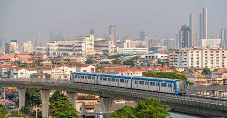 City metro train carriage departs over an overpass bridge to the central part of the metropolis, tall skyscrapers are visible in the distance