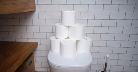 Stack of toilet paper stands on white toilet in bathroom. Toilet paper selection concept