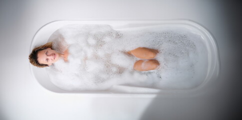 Young woman lying in warm bath with foam top view. Body care concept