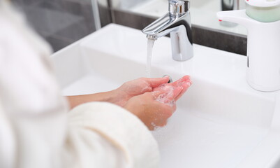 Woman washing her hands under water from tap in bathroom closeup. Hand hygiene concept