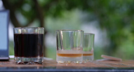 Two transparent glass glasses full of dark liquid and empty stand on table. Drinking drinks in...