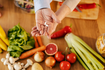Senior couple hands holding vitamins and pills with vegetables in a blurry background.