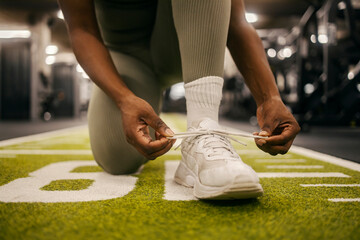 Close up of a black sportswoman's hands typing shoelace at gym.