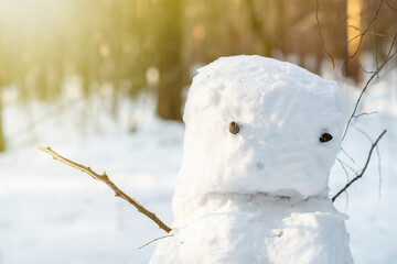 A clumsy, sad snowman among the trees in the forest. Sunny winter background in the park.