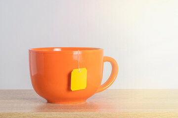 A tea bag with a blank yellow label in a cup. Cozy template with space for text on a tea bag tag.