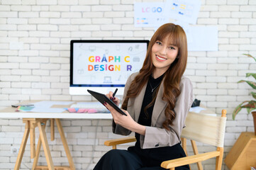 Asian female artist drawing something on graphic tablet. graphic designer working at office. Looking at camera.