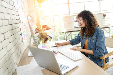 Portrait of attractive female graphic designer sitting at desks and drawing artworks on paper. Creative people work in office with computer graphics and laptops.