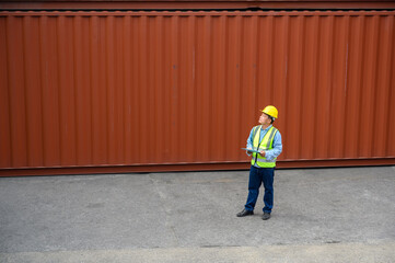 Foreman or Engineer wears yellow helmet and reflection shirt to control or check inventory details of containers box. Container loading cargo freight in import and export business logistic industry.