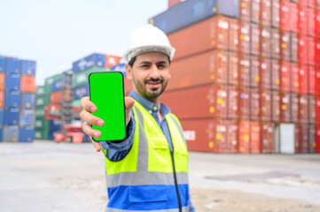 Logistic operators worker shows mock up mobile phone with blank screen, working in cargo container warehouse industry factory site in export, import, and transportation concept.