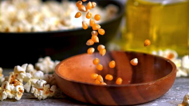 Popcorn is being transferred from a bag into a wooden bowl on a table. The snack is ready to be enjoyed with a drink or while watching a movie