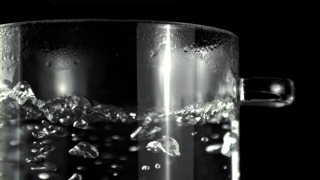 A glass of water is boiling in a pot on a black background, creating steam. The liquid in the highball glass is heating up in the barware