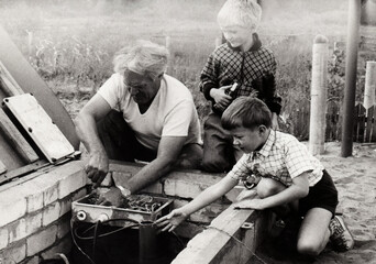 A grandfather teaches his grandchildren how to repair a water supply pump from a well. Vintage...