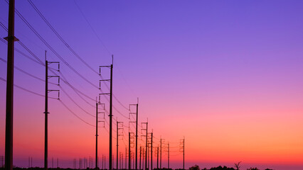 Silhouette two rows of electric poles with cable lines on curve country road against colorful...