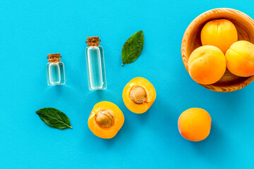Apricot kernel oil among apricots and leaves on blue background top view pattern