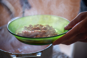 man serving hot chickpeas in green glass dish, steaming legumes on the plate against the light in a rustic space, middle-aged man's hands