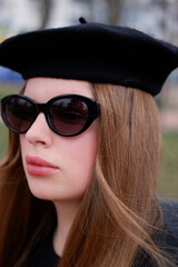 young blonde in a black beret and black glasses. woman in a beret and glasses, portrait photo of a blonde. Woman outdoors wearing sunglasses