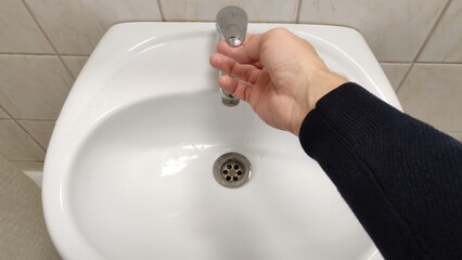 Man opens the faucet in the bathroom