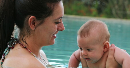 Mother holding baby son inside swimming pool water interaction