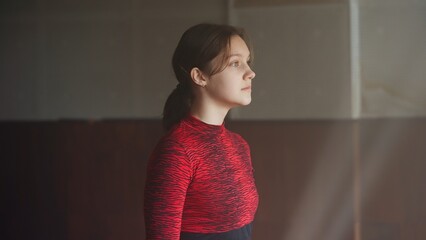Portrait of a young girl dancer in a red topcoat, looking into the distance. Side view of the girl...