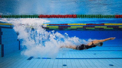 Female swimmer in water immersion phase, entering and sliding below the water surface making...