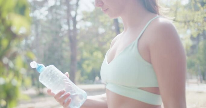 Healthy young female athlete drinking water from a bottle after exercise, staying hydrated on a sunny day.