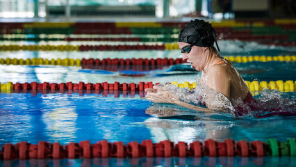 Female swimmer using breaststroke technique to swim an indoor lap pool. Competitive swimming...