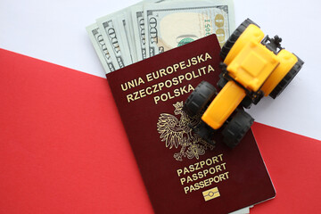 Red polish passport and yellow tractor on US money and smooth red and white flag of Poland close up - obrazy, fototapety, plakaty