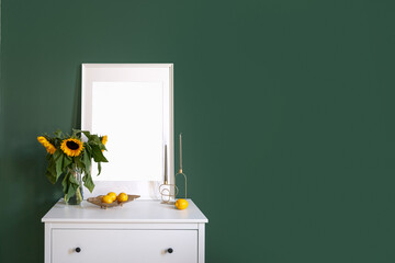 White commode with picture and vase with flowers against green wall in bedroom