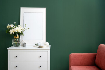 White commode, picture in frame and vase with flowers on green wall background
