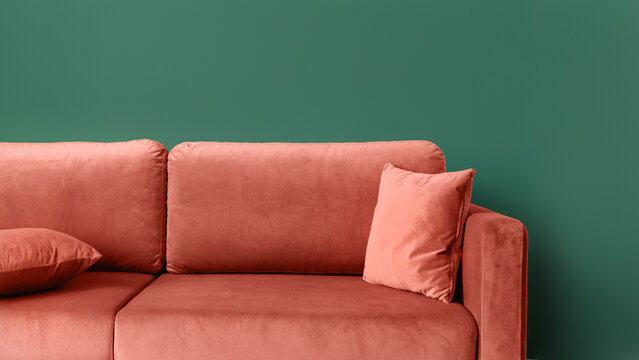 Close up of coral comfortable couch with cushions against green wall