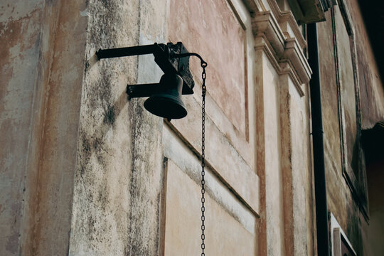 Antica campana in bronzo scuro montata sulla facciata storica di una chiesa o palazzo d'epoca con catena in ferro e intonaco antico rovinato dal tempo