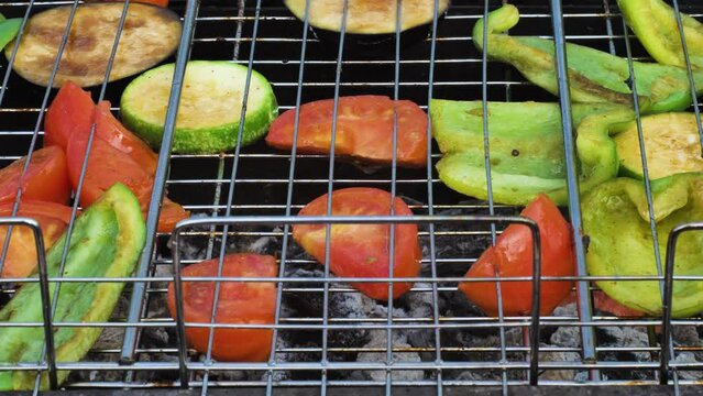 Close-up of fresh tomatoes, aubergine, zucchini and peppers roasting on a barbecue. The vegetables show signs of charring. Cooking healthy food on coals