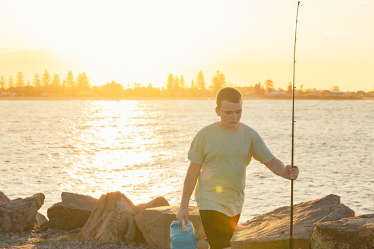 Boy with fishing equipment on the Stockton breakwall in golden afternoon light