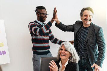 Diverse group of multicultural colleagues shares a high five the office, celebrating a collective...