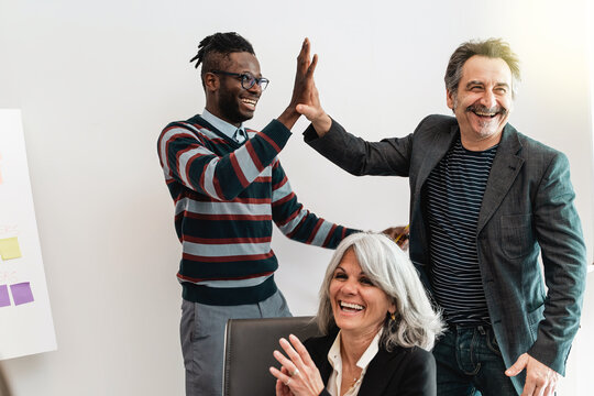 Diverse group of multicultural colleagues shares a high five the office, celebrating a collective achievement with joy and multiethnic inclusivity, reflecting a culture of teamwork and mutual support.