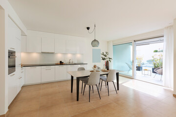 Large kitchen with dining table inside. Modern space and a window opening onto a terrace.