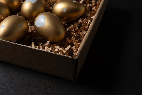 Gold eggs in paper box on black background.
