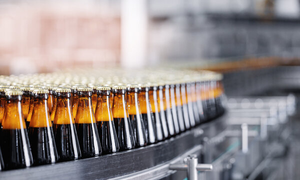 Automated modern beer bottling factory line with glasses bottles on conveyor. Banner Brewery industry food manufacturing, sunlight