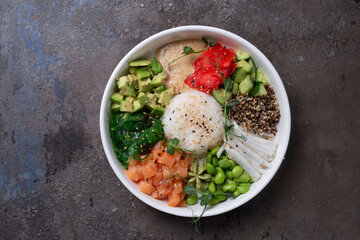 Top view of a bye bowl with salmon, avocado, cucumber, sprouts and rice on a white plate